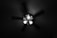 A ceiling fan is captured from below, with three light fixtures attached. The fan blades are blurred, suggesting motion, while the central light illuminates the surrounding area.