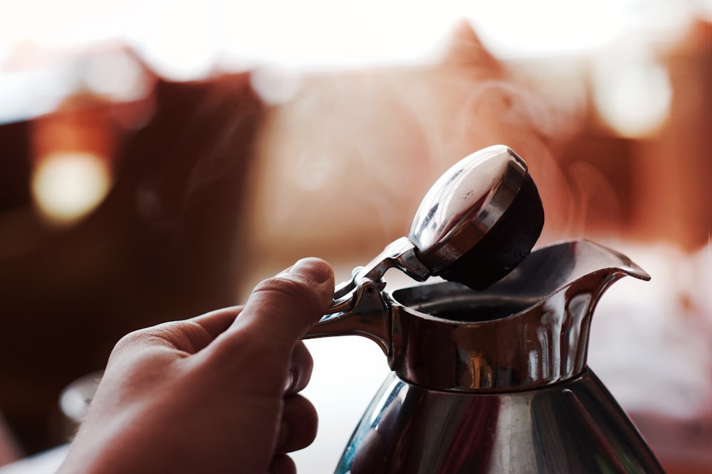A coffee pot being held and opened to allow steam to escape