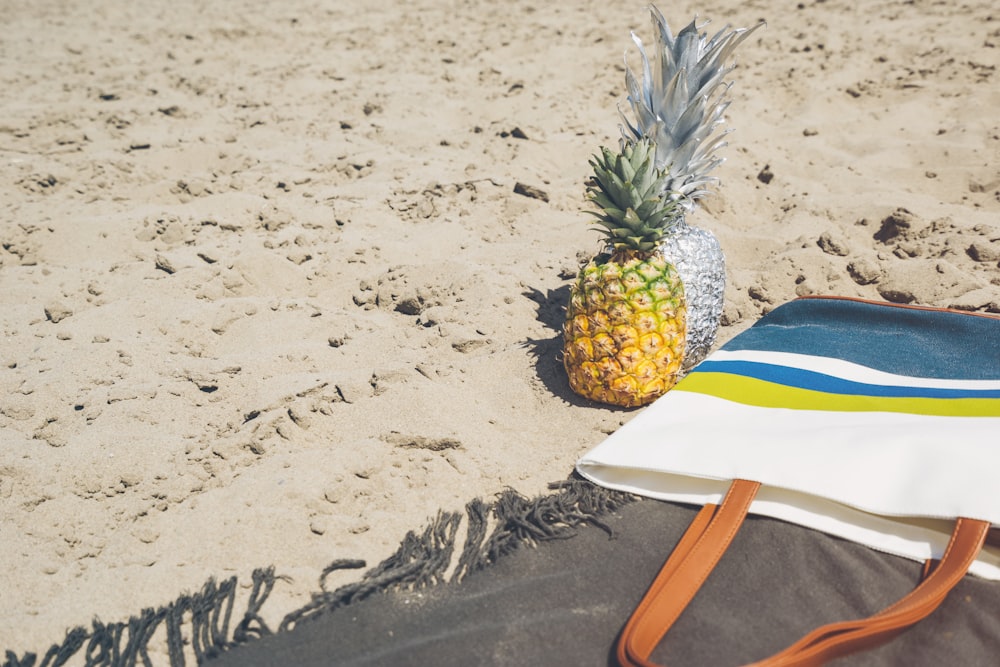 a pineapple sitting on top of a beach next to a bag