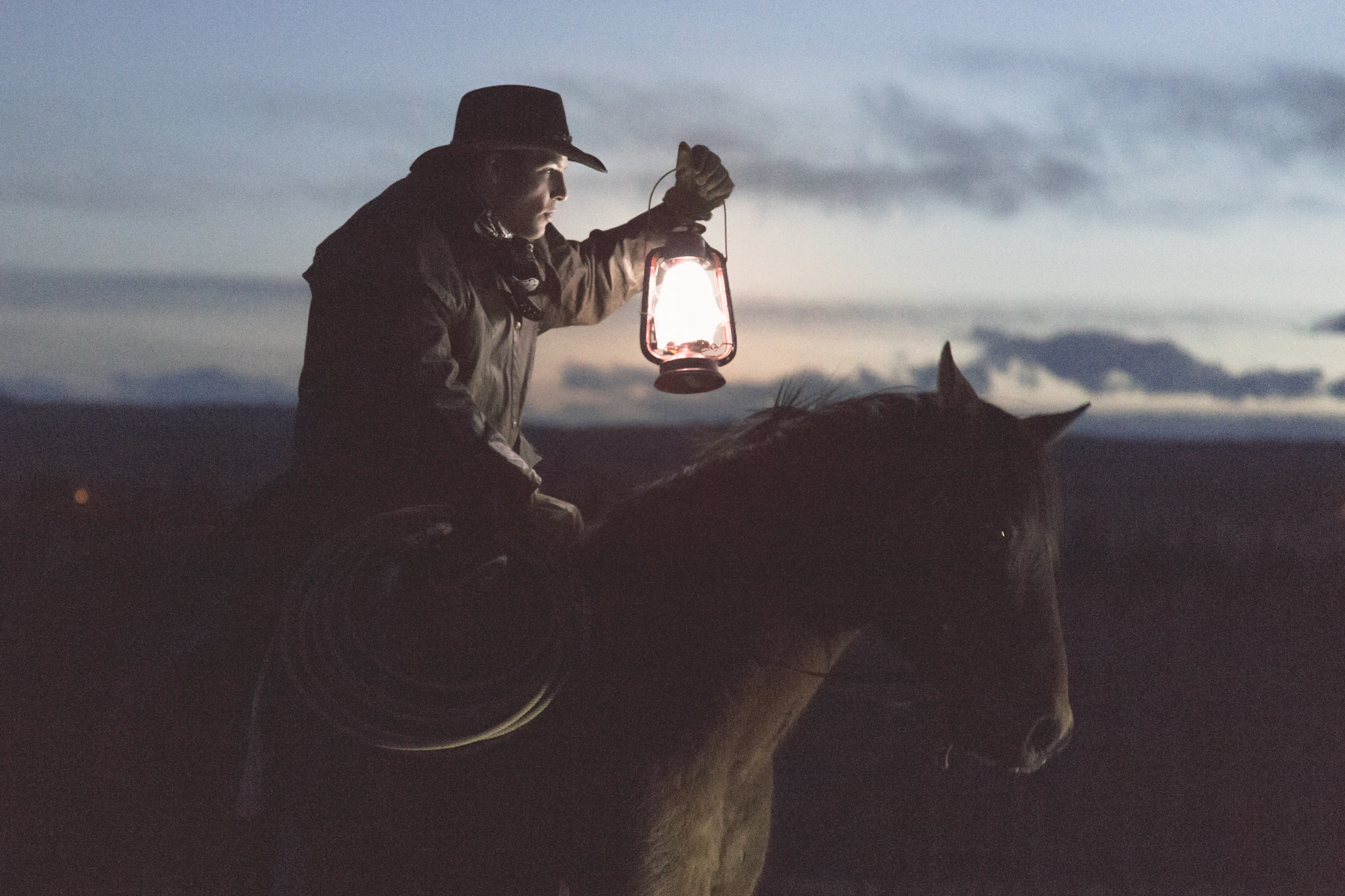 Rider on horseback holding a lantern at dusk near Carstairs, Mountain View County