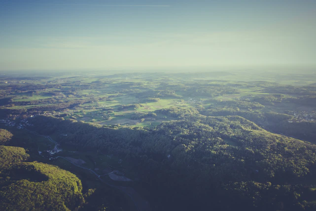 A stunning aerial view of lush green land plots under a clear blue sky, highlighting open space and natural beauty.