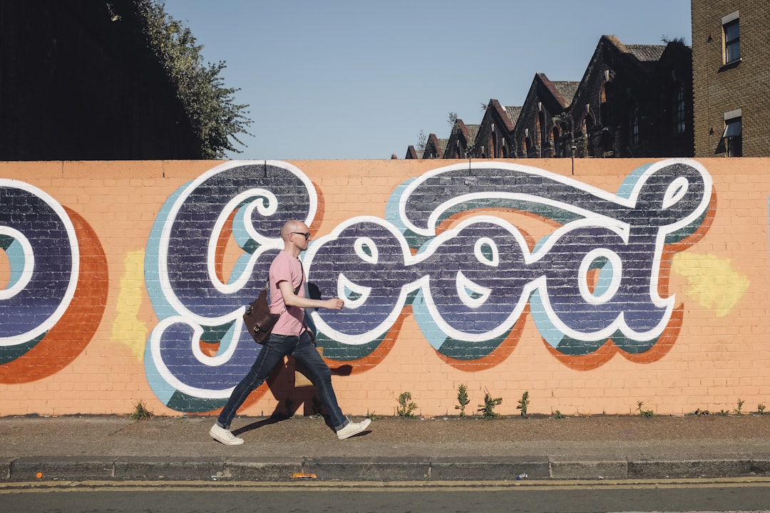 man walking beside graffiti wall, Bald man walks in front of graffiti