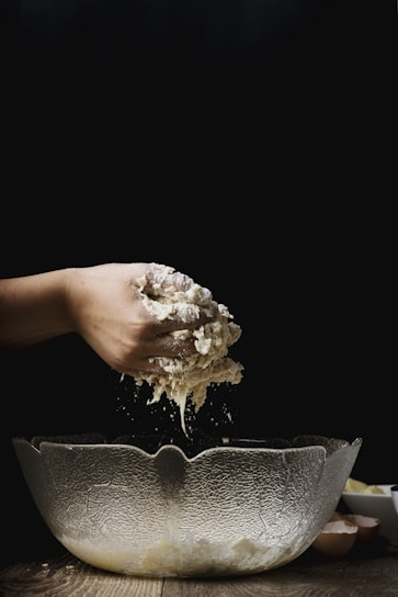 Close-up of hands mixing organic flour and eggs in a rustic bowl on a farmhouse kitchen counter.