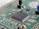 A close-up view of a green printed circuit board featuring various electronic components, including an integrated circuit chip marked with identification codes, resistors, and connectors. The board is intricately designed, showing numerous paths and soldered points.