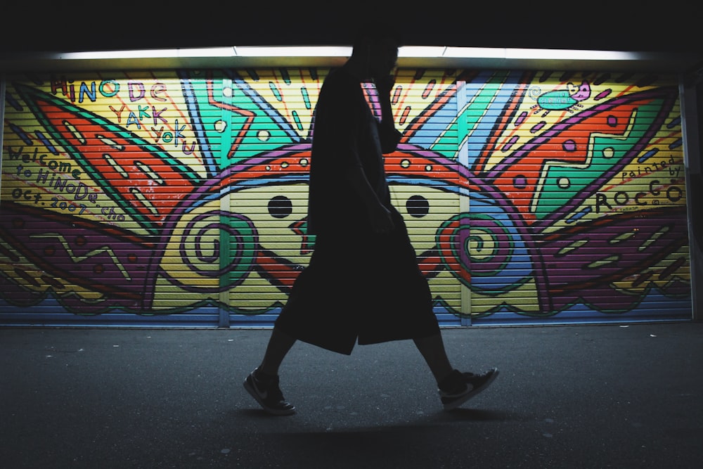 silhouette photo of a man wearing shorts standing near painted roller shutter