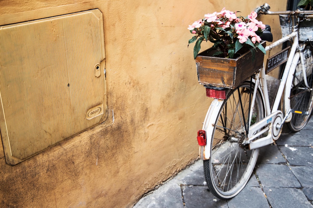 white bicycle with potted flower beside yellow wall