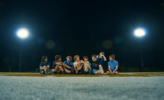 A lively group of college students sharing burgers and fries under bright stadium lights.