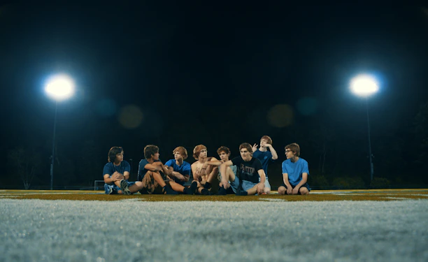 A lively group of college students sharing burgers and fries under bright stadium lights.