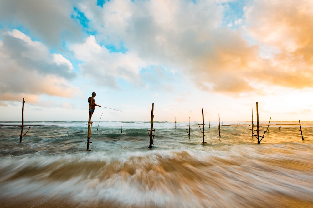 person fishing while standing on brown wooden post during daytime