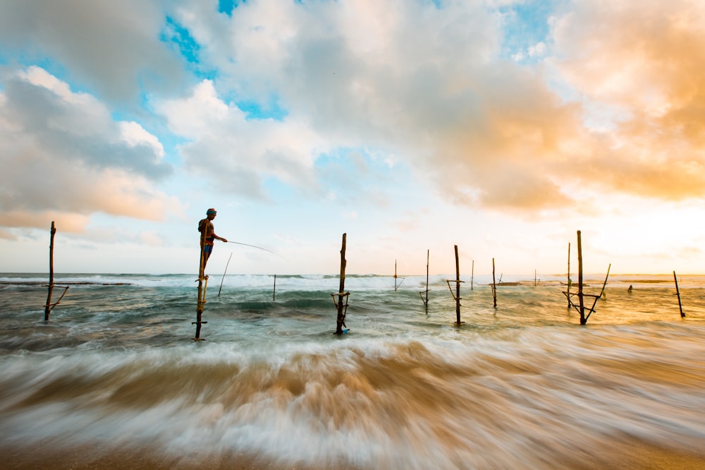pessoa pescando em pé em poste de madeira marrom durante o dia