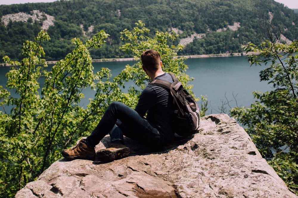 person with backpack sitting on gray rock