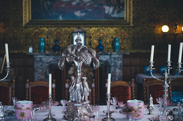 a large dining table with opulent place settings, a silver statues, and swith a luxuriously-appointed wall in the background