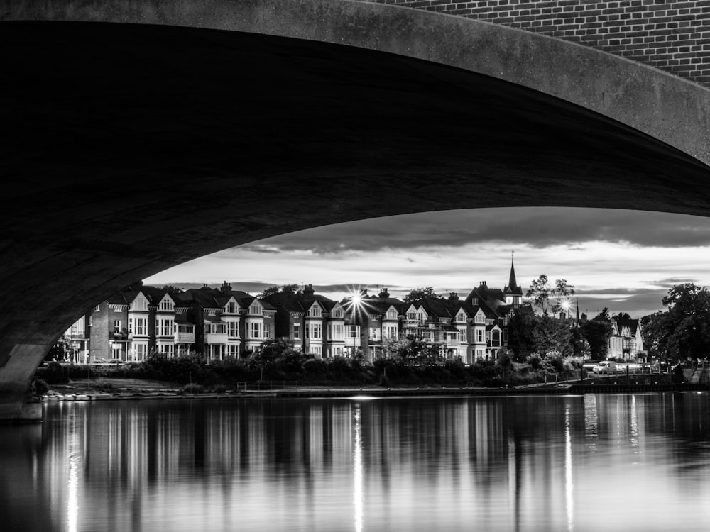 grayscale view of building under bridge across water