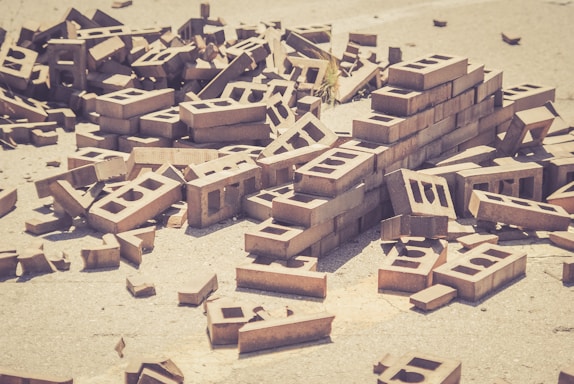 A pile of scattered bricks is strewn across a concrete surface. The bricks are in various orientations, with some stacked neatly while others are haphazardly arranged.