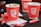 Three red paper cups with the 'Café Coffee Day' logo are placed on a tray. There are also several empty sugar sachets scattered around on white napkins.