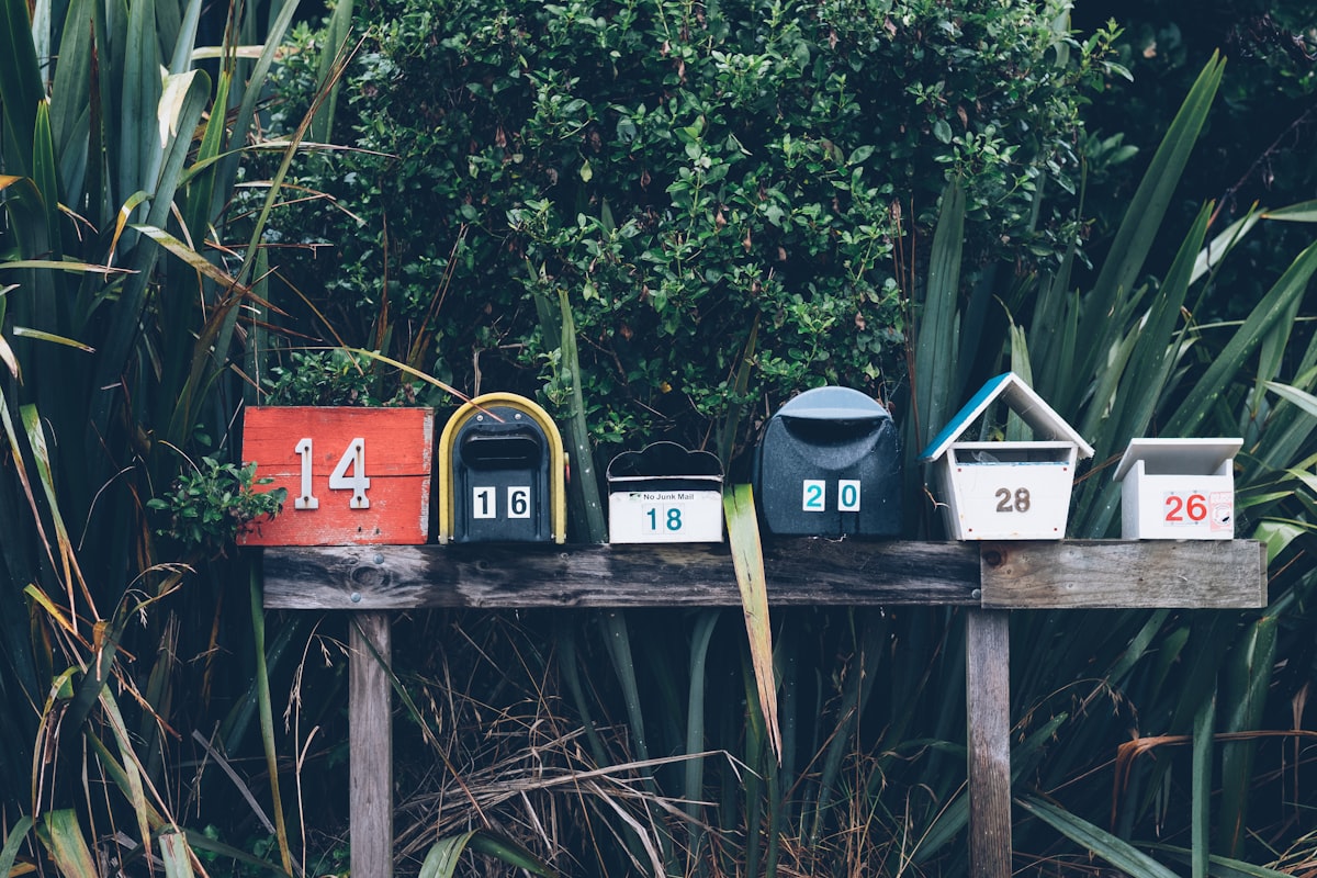 Six assorted-color mailboxes nestled in greenery, neighborhood register