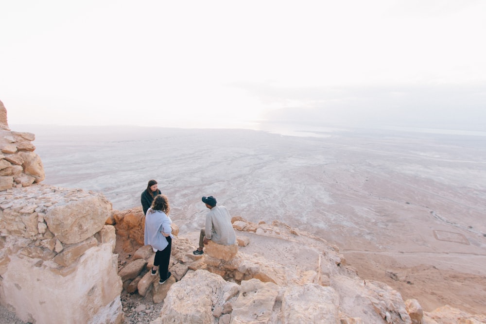 three person on cliff under white sky