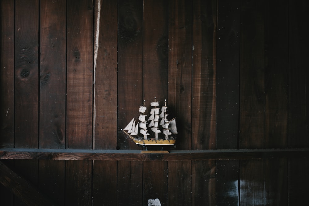 Modelo em escala de navio galeão preto, marrom e branco em prateleira de madeira marrom