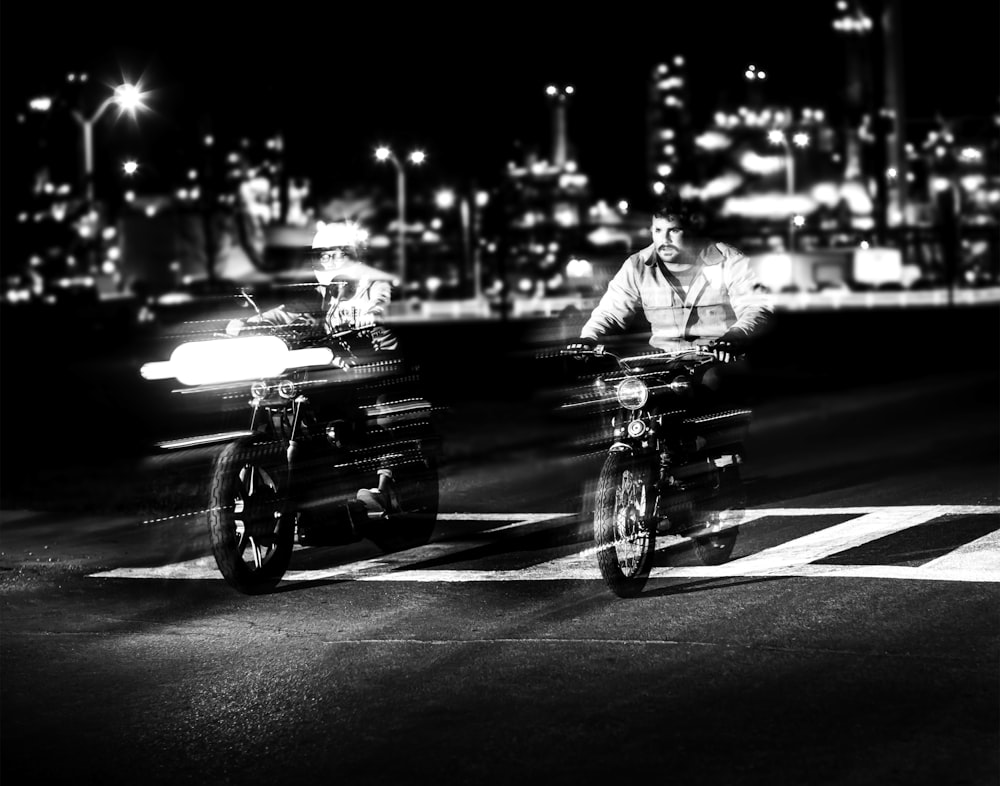 grayscale photo of person riding motorcycle near building and street lights