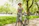 A smiling young woman in workout gear, holding a phone with the vigora app open, standing in a sunlit park.