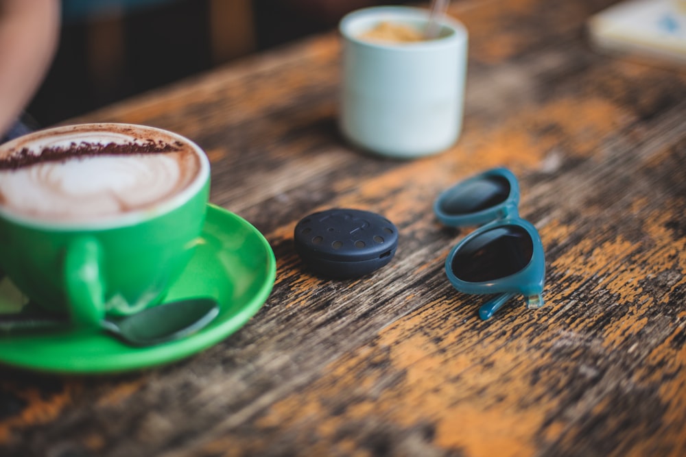 ceramic mug on saucer beside sunglasses