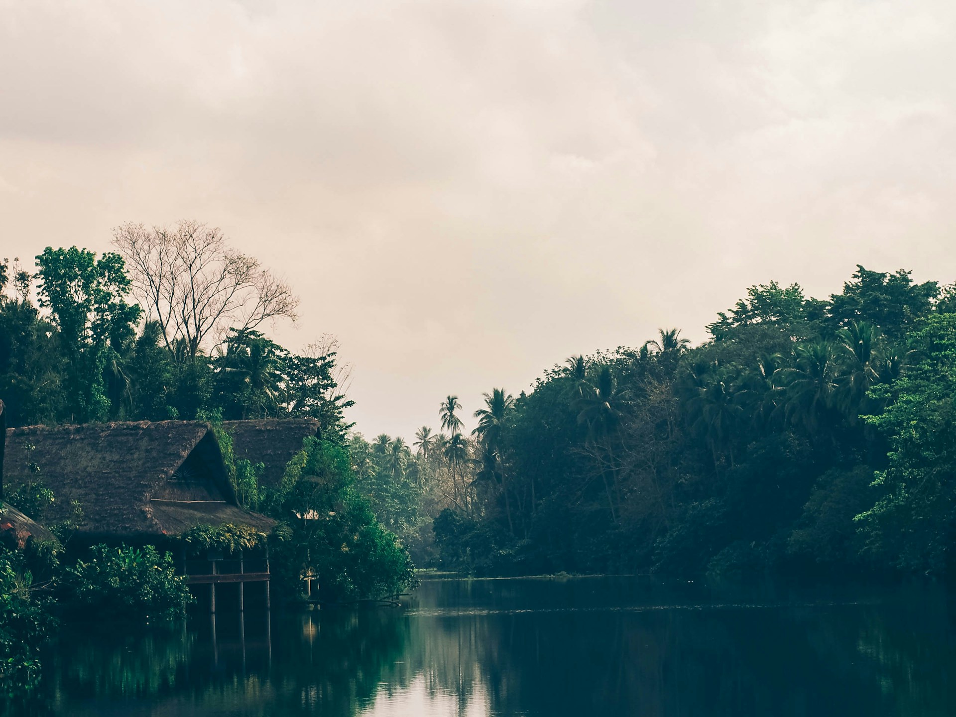 Sunrise over the serene Ganges river with the cozy cottages of Rishikesh Resort nestled among lush green hills.