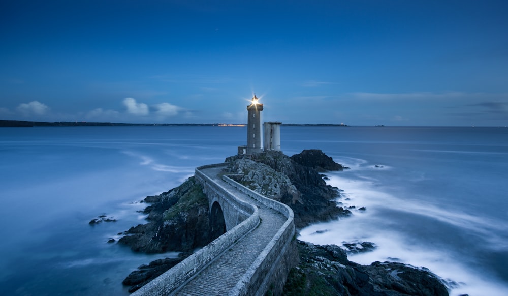 gray lighthouse on islet with concrete pathway at daytime