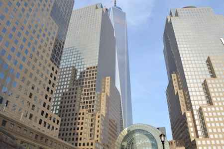 Tall skyscrapers with reflective glass façades rise into the blue sky, bordered by a modern architectural structure with a dome. The symmetry and grid-like patterns of the buildings create a sense of modern urban development.
