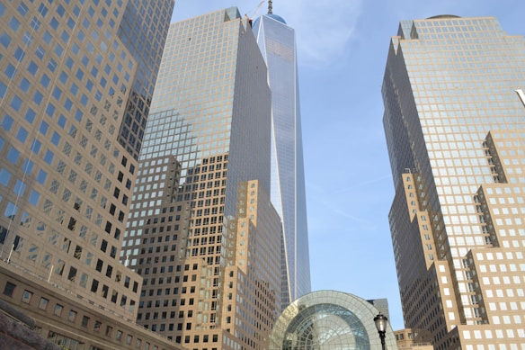 Tall skyscrapers with reflective glass façades rise into the blue sky, bordered by a modern architectural structure with a dome. The symmetry and grid-like patterns of the buildings create a sense of modern urban development.