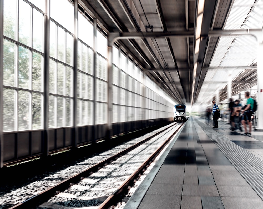 Zeitrafferfoto eines Zuges, der tagsüber auf dem Bahnhof mit Menschen daneben fährt