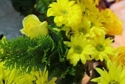 A bouquet of bright yellow flowers mixed with lush green foliage. Prominently featured are chrysanthemums and a single rose, their vibrant petals contrasting against the greenery. The arrangement appears fresh and lively.