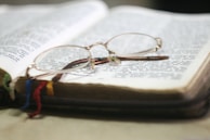 Close-up of an open book with highlighted passages and a pair of reading glasses resting on top.