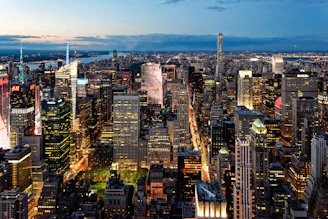 A vibrant cityscape at dusk with glowing windows and bustling streets below.