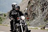 Motorcycle enthusiasts wearing custom embroidered jackets on a curvy mountain road.