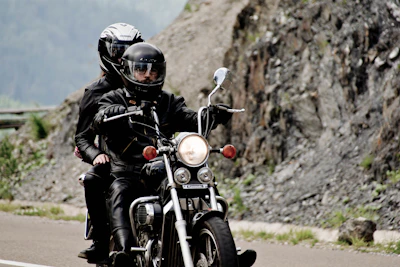 Motorcycle enthusiasts wearing custom embroidered jackets on a curvy mountain road.
