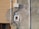 An exterior wall section showcasing various electrical conduits and a junction box attached to a textured surface. The wall has patches of paint in different shades and the sunlight casts shadows accentuating the details of the wall and conduits.