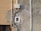 An exterior wall section showcasing various electrical conduits and a junction box attached to a textured surface. The wall has patches of paint in different shades and the sunlight casts shadows accentuating the details of the wall and conduits.