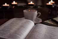 A vinscent candle resting on a wooden tray beside a steaming cup of tea and an open book.
