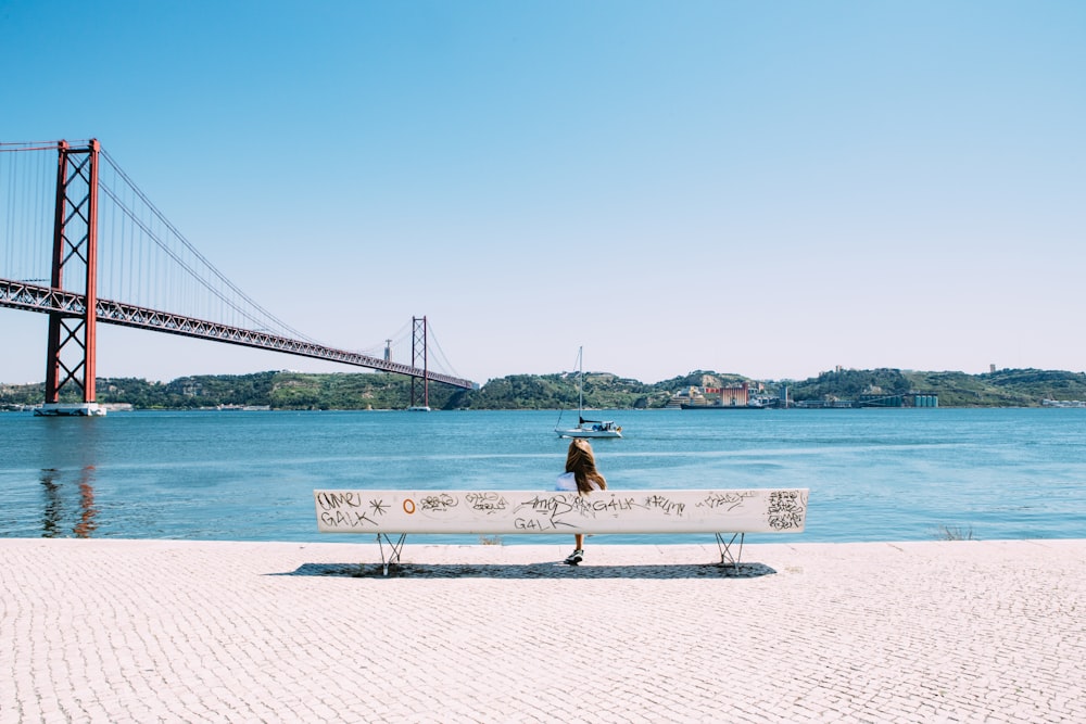 woman sitting on white bench in front of sea