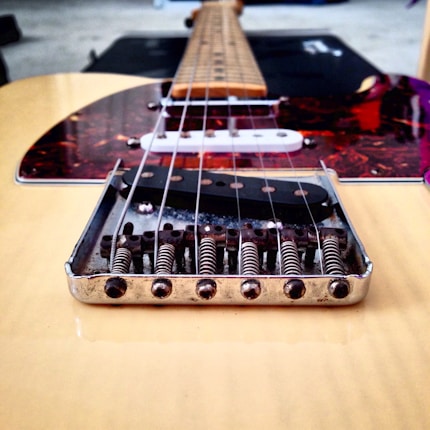 Close-up view of a guitar bridge with visible springs and metal components. The strings run vertically towards the neck, and the body has a shiny, polished finish. Parts of the pickguard and pickups are visible, adding to the intricate detailing.