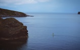 Sunlit aerial capture of a paddleboarder gliding over calm sea near rocky shore