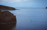 A vibrant paddle boarder balancing skillfully near a rocky shoreline.
