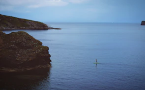 A vibrant paddle boarder balancing skillfully near a rocky shoreline.