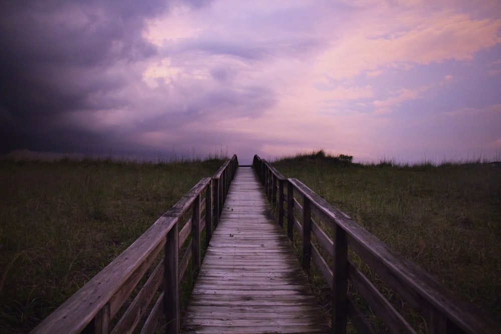 brown wooden bridge over green grass field under white clouds