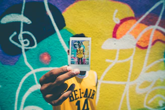 person holding printed photo of him with graffiti as background