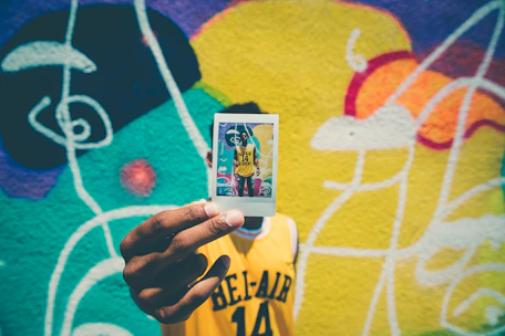 person holding printed photo of him with graffiti as background