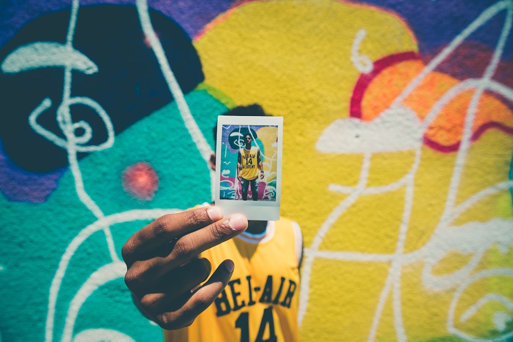 person holding printed photo of him with graffiti as background