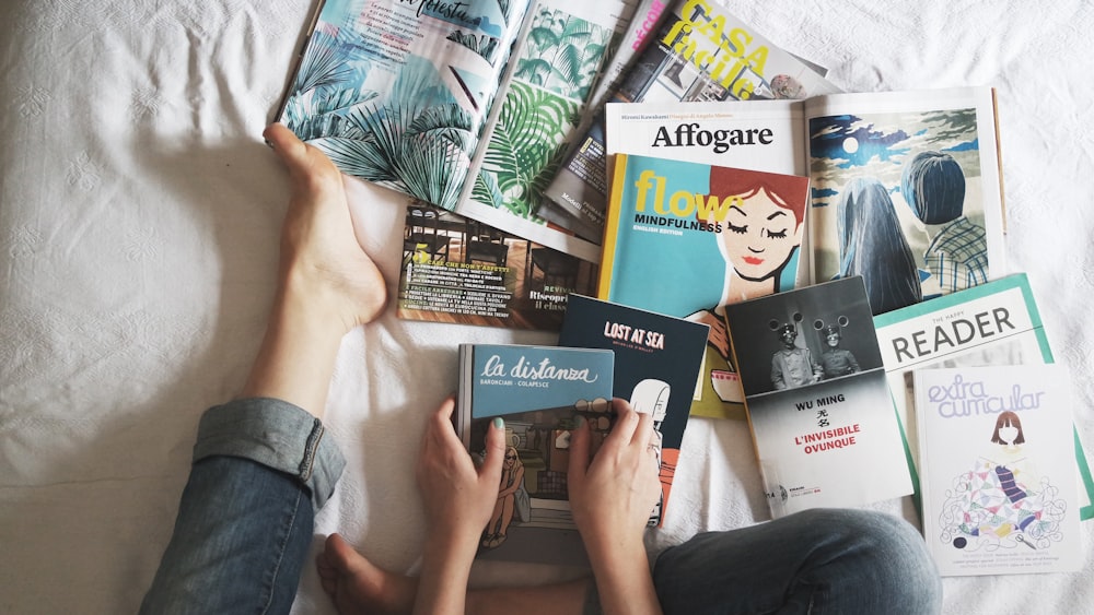 A woman sitting on her bed in jeans looking at several books and magazines in Milan