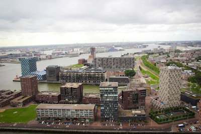 Aerial view of an urban landscape featuring water channels, modern apartment buildings with geometric designs, and surrounding industrial structures. The area is characterized by diverse architectural styles and a mix of green spaces, roads, and residential blocks.