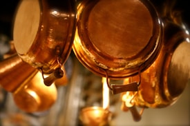Hanging copper pots and pans, showcasing their polished surface and warm metallic hues. The focus is on the intricate details and reflections, with a soft background blur.